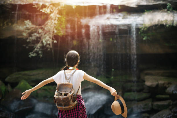 joven sentada frente a la cascada con levantar los brazos - waterfall zen like women meditating fotografías e imágenes de stock