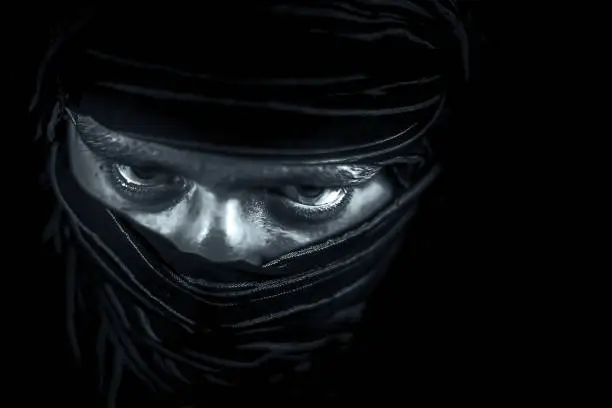 Striking portrait of male teenager isolated on black with piercing expressive eyes along with a cloth covering face except eyes.Expressing boldness and Courage.