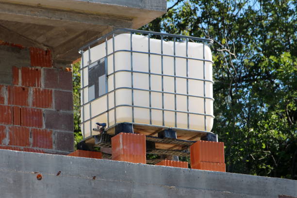 белый промежуточный навалом контейнер или ibc пластиковый бак с металлической клеткой положить на вершине красных строительных блоков на м� - intermediate стоковые фото и изображения
