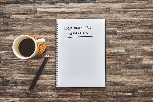 Shot of coffee, stationary and a notebook with the words “2020 new year's resolutions” written on it