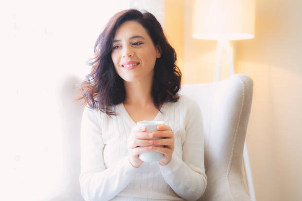 istock beautiful woman drinking coffee in the morning sitting by the window 1182876708