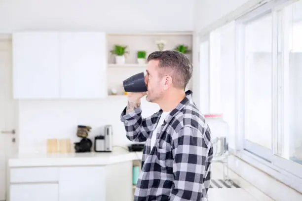 Side view of Caucasian man drinking a cup of coffee while standing in the kitchen