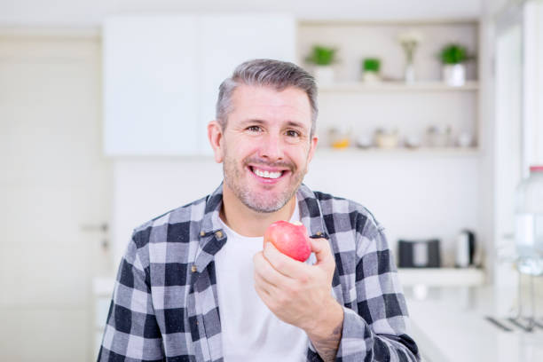 istock Smiling Caucasian man eating an apple in kitchen 1182877834