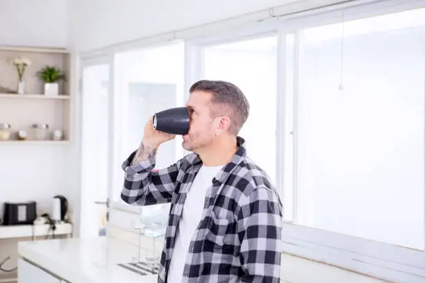 Portrait of young man drinking a cup of coffee while standing in the kitchen
