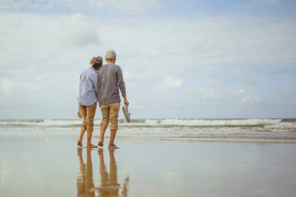 Senior couple walking on the beach holding hands at sunrise, plan life insurance at retirement concept. stock photo