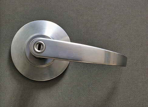 Plain modern silver door handle isolated on a solid gray door with key lock.