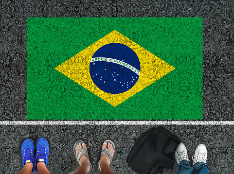 people legs are standing on asphalt road next to flag of Brazil and border
