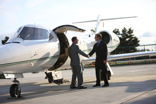 Young corporate businessman walking on tarmac toward private jet plane\nThe pilot greets him, welcome aboard