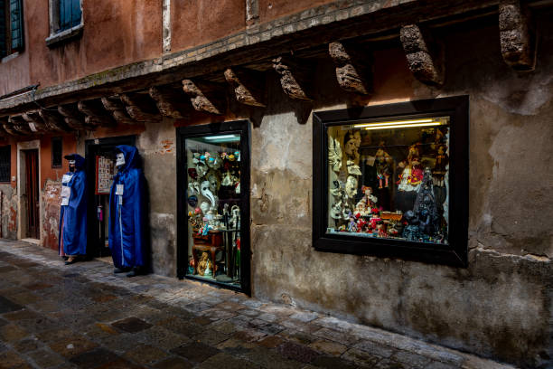 Candid image of colourful masks in a gift shop window in Venice, Italy. This is the exterior of the shop with caped masquerade mannequins either side of the doorway.