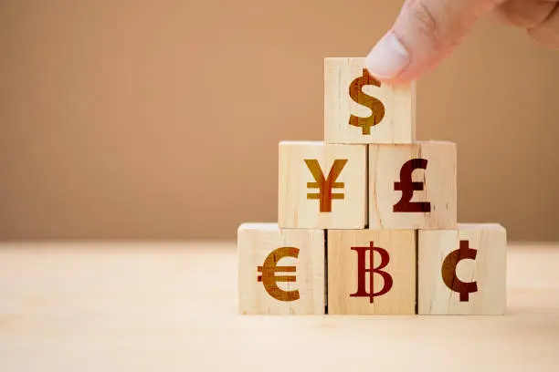 Photo of Hand putting wooden cube of US dollar sign to Yuan  Yen Euro and Pound sterling sign.US dollar is main and popular currency of exchange in the world.Investment and saving concept.