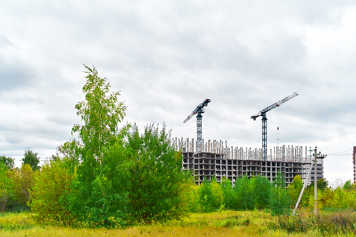 Construction site, building a new house, cranes, autumn yellow green trees, cloudy sky