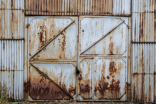 Closed old rusty iron gate sash in a corrugated iron wall. Abandoned industrial building. Grunge