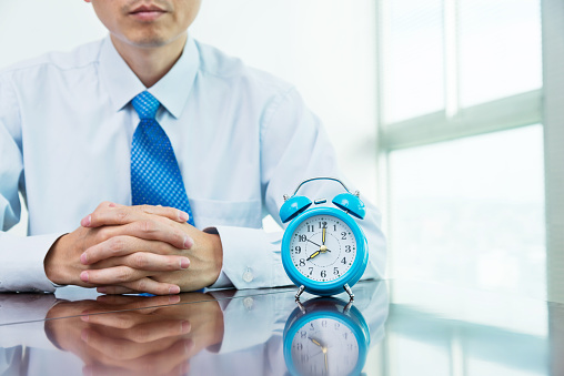 Businessman sitting in front of the desk with an alarm clock.