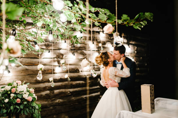 마법의 밤 숲에서 결혼식 부부는 빛 화환을 장식. 등불과 램프장식으로 꽃을 장식한 의식. 전구 조명의 배경에 신부와 신랑 키스. - bride caucasian wedding ceremony close up 뉴스 사진 이미지