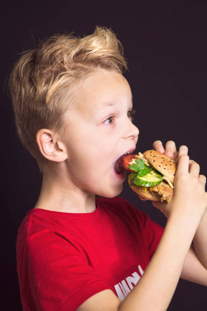 istock funny boy close-up with open mouth eats a delicious burger with chicken 1182892681