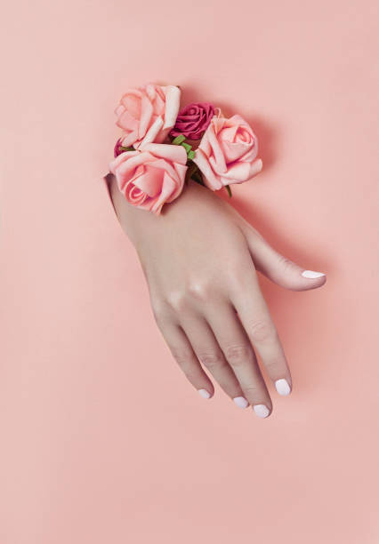 istock Hand with paper flowers and painted nails is thrust through a hole in the paper background. Cosmetics and hand care, moisturizing and wrinkle reduction 1182895426