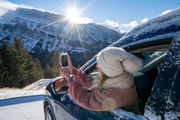 istock Woman inside car in winter using mobile phone, snowcapped mountains 1182898235