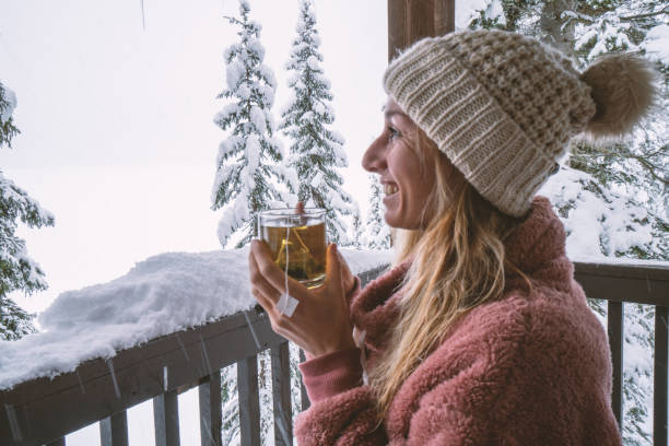 istock Woman in log cain looking at the snow falling with tea cup in hands 1182901191