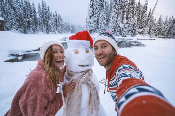 It's Christmas time - Couple taking selfie with snowman on winter vacations Christmas time; Young couple taking selfie with snowman in snowy mountain landscape; having fun in winter vacations yoho national park photos stock pictures, royalty-free photos & images