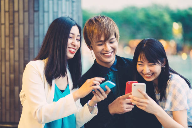 Young japanese people enjoying modern technologies Group of friends using smartphones outside kinki region stock pictures, royalty-free photos & images