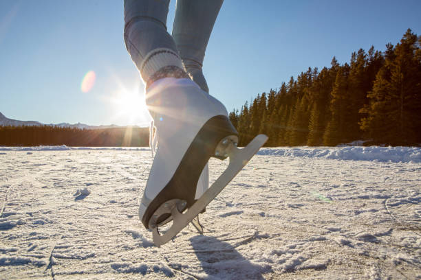 楽しんで冬休みを楽しむ夕暮れ時の凍った湖での女性アイススケートの背面図 - rocky mountains canada mountain winter ストックフォトと�画像