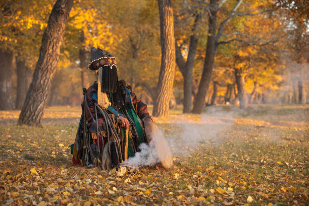 Mongolian traditional shaman performing a traditional shamanistic ritual with a drum and smoke in a forest during autumn afternoon. Ulaanbaatar, Mongolia.