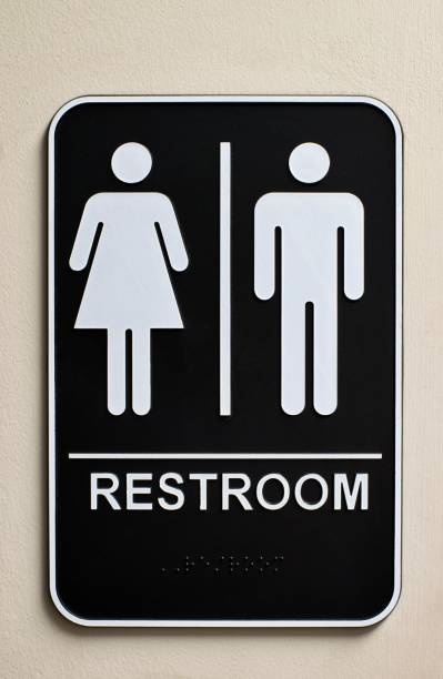 Unisex bathroom sign on a wall. Vertical restroom sign on a wall for a unisex bathroom with male and female icons, braille at the bottom and no handicap icon. outhouse interior stock pictures, royalty-free photos & images