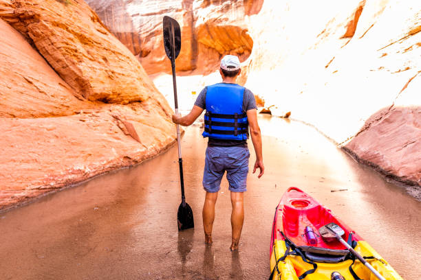 Kayaking hiking trail in Lake Powell narrow and shallow antelope canyon with man holding paddle oar standing in dirty muddy water and rock formations Kayaking hiking trail in Lake Powell narrow and shallow antelope canyon with man holding paddle oar standing in dirty muddy water and rock formations glen canyon stock pictures, royalty-free photos & images