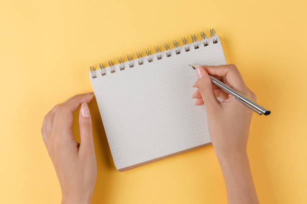 istock girl writes in an open notebook top view, yellow background 1182911457