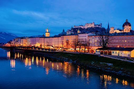 Panorama of Salzburg Hohensalzburg castle and Salzach River in Austria in evening. Landscape and cityscape of fortress in Mozart city in Europe at winter at night. View of old Austrian town