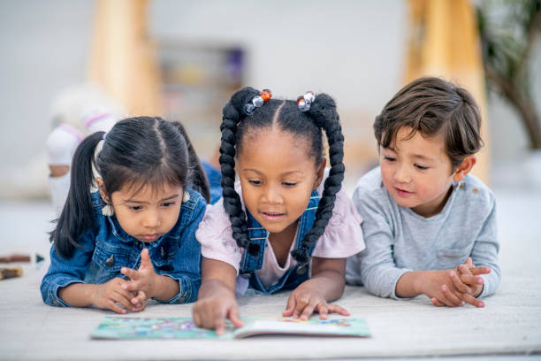 grupa trzech wieloetnicznych dzieci leżała na podłodze czytając razem zdjęcie stockowe - preschool child preschooler multi ethnic group zdjęcia i obrazy z banku zdjęć