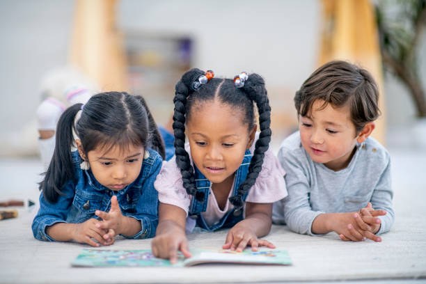 um grupo de três crianças multi-ethnic colocam na leitura do assoalho junto foto de stock - preschool child preschooler multi ethnic group - fotografias e filmes do acervo
