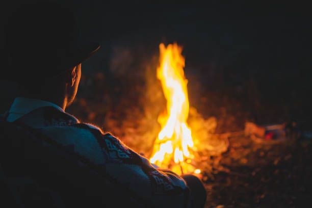 Man in traditional native american poncho and hat sits by the fire in the wood