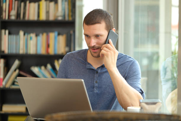 istock Serious man talks on phone and uses a laptop 1182917505