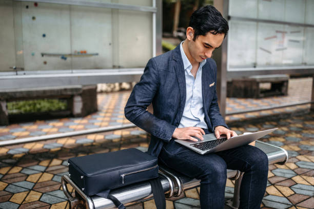 istock Businessman using laptop at bus stop 1182917939