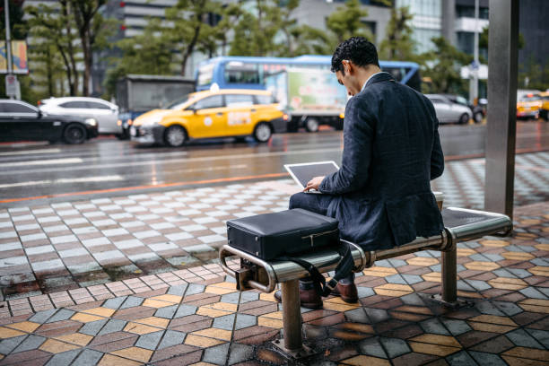 istock Businessman using laptop at bus stop 1182918032