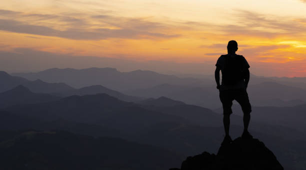 istock man on top at sunset surrounded by mountains 1182918050