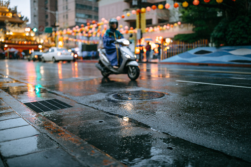Unrecognizable person riding motorcycle on wet road in rainy season