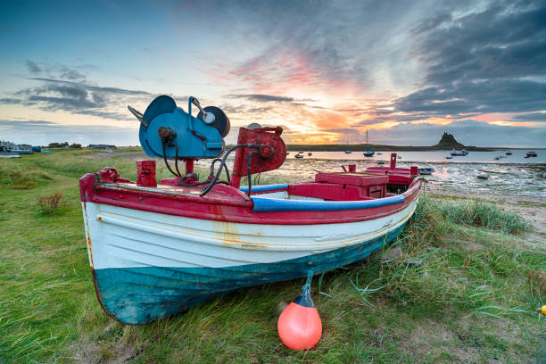 Holy Island of Lindisfarne, United Kingdom - February 1, 2015: Lindisfarne Castle is in the background behind former fishing boats now used as storage sheds  by the fishermen on Holy Island, Northumberland.