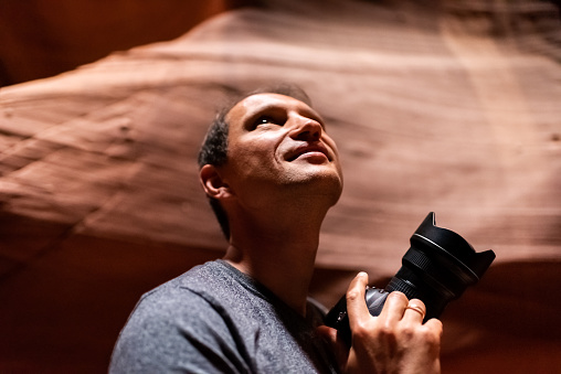 Young man inside Upper Antelope slot canyon in Arizona taking pictures with camera of sandstone formations looking up