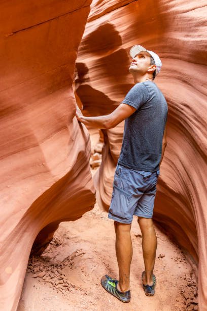 orange red wave shape formations with man walking touching looking back up at narrow antelope slot canyon in arizona on path footpath trail from lake powell - 16637 imagens e fotografias de stock