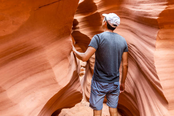 istock Orange red wave shape abstract formations rocks with man walking touching narrow Antelope slot canyon in Arizona on path footpath trail from Lake Powell 1182930195