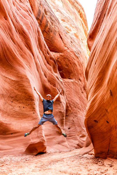 randonneur heureux d'homme sautant vers le haut de la vue verticale par des formations rouges de forme d'onde au canyon de fente d'antelope en arizona sur le sentier de sentier du lac powell - 16621 photos et images de collection