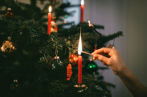 female hand lighting red candle on christmas tree at christmas eve