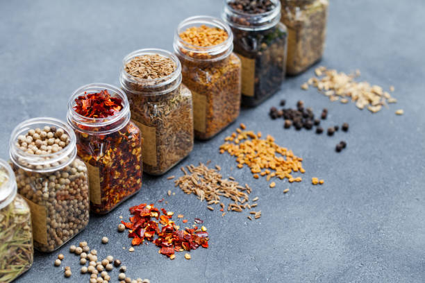 Assortments of spices, white pepper, chili flakes, lemongrass, coriander and cumin seeds in jars on grey stone background. Copy space. stock photo