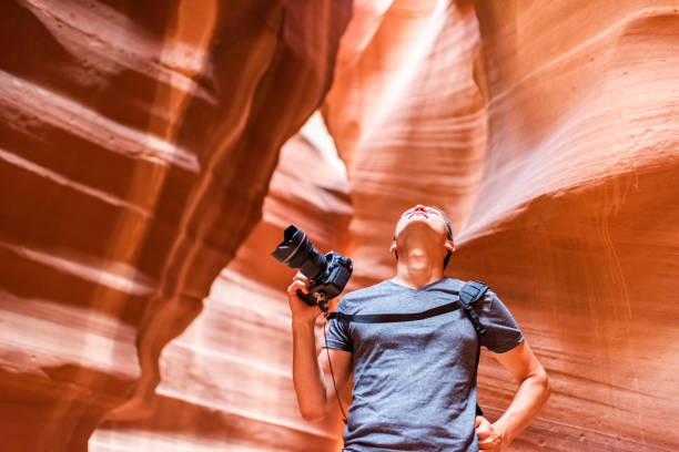 garganta do entalhe do antílope com a câmera de terra arrendada do homem do fotógrafo que olha acima em formações abstratas de arenito vermelho das camadas da rocha alaranjada na página, o arizona - desfiladeiro antelope canyon superior - fotografias e filmes do acervo