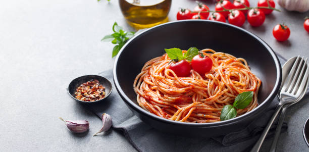 Pasta, spaghetti with tomato sauce in black bowl on grey background. Copy space.