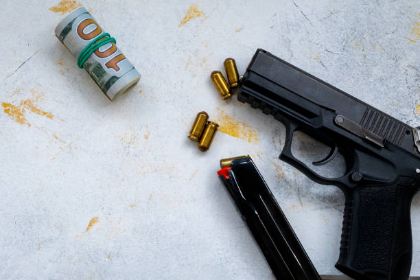 istock 9 mm pistol gun bullets strewn and roll american dollar banknotes on rustic oak table. 1182939723