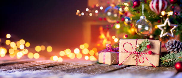 christmas home room - gift box below tree with lights and fireplace - christmas present imagens e fotografias de stock