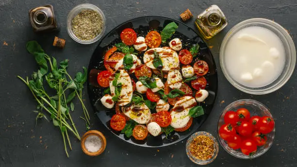 Ingredients for italian caprese salad. Mozzarella balls, tomatoes, basil leaves, olive oil with balsamic vinegar over concrete background
